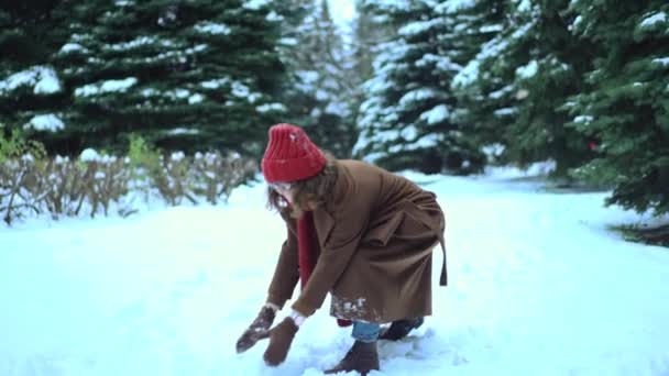 Jovem mulher bonita em cachecol de malha e chapéu jogando bolas de neve no parque. Moda de inverno — Vídeo de Stock