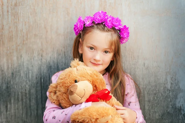 Portret van schattig meisje met heldere roze bloem hoofdband, houden teddybeer close-up — Stockfoto