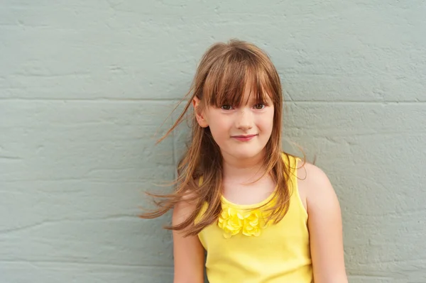 Ulkona lähikuva muotokuva suloinen pieni tyttö 6-7 vuotta vanha, yllään kirkkaan keltainen alkuun — kuvapankkivalokuva