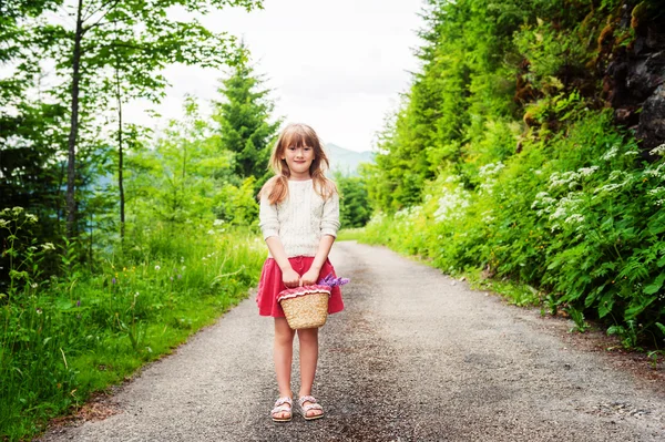 베이지색 스웨터와 빨간색 치마를 입고 꽃, 작은 바구니를 들고 6-7 년 오래 된 숲, 하이킹의 귀여운 꼬마 소녀 — 스톡 사진