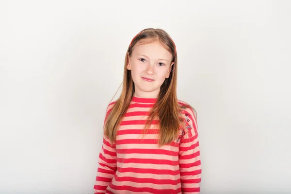 Retrato de estudio de una adorable niña de 8-9 años, vistiendo jersey de rayas de color coral, de pie sobre fondo blanco — Foto de Stock