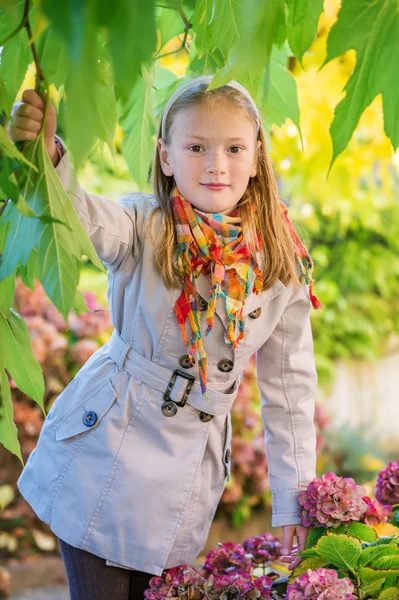 Outdoor portrait of a cute little girl of 8 years old, wearing beige coat and colorful scarf — Stock Photo, Image