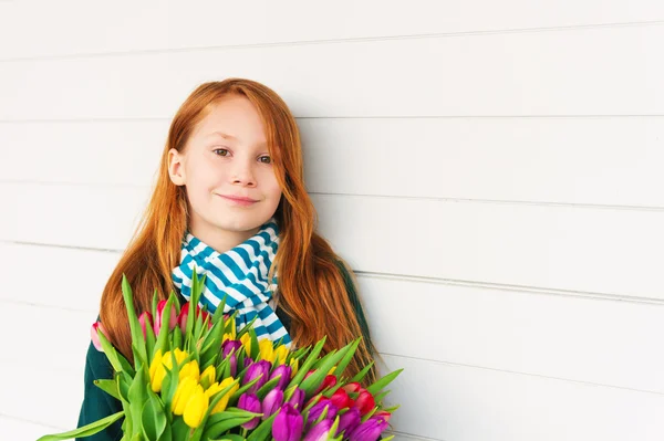 Portrait of redhead girl of 8-9 years old, holding bright bouquet of colorful fresh tulips, standing against white wooden background — Stock Photo, Image