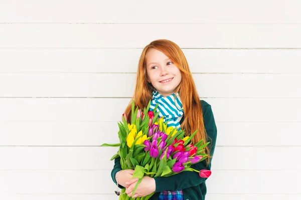 Portrait of redhead girl of 8-9 years old, holding bright bouquet of colorful fresh tulips, standing against white wooden background — Stock Photo, Image