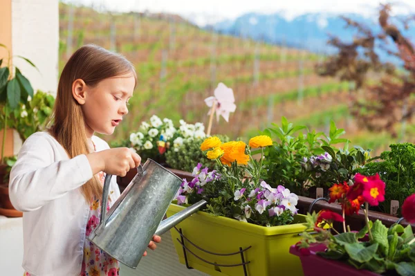 Adorable little girl watering flowers on the balcony — Stock Photo, Image