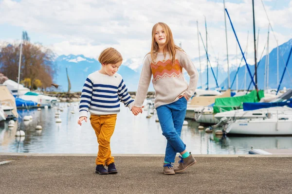 Two adorable kids playing by the lake in early spring, wearing pullovers and colorful trousers — Stock Photo, Image