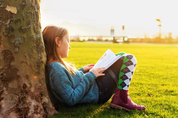 Adorable little girl reading book in the park at sunset — Stock Photo, Image