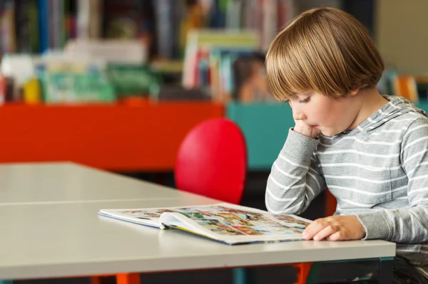 Little preschooler boy of 5 years old reading book in the library — Stock Photo, Image