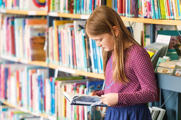 Mała dziewczynka czyta książkę w bibliotece — Zdjęcie stockowe