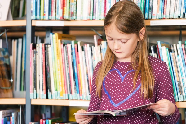 Mała dziewczynka czyta książkę w bibliotece — Zdjęcie stockowe