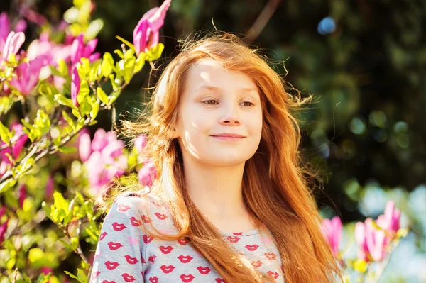 Outdoor portrait of adorable little redhead girl with magnolia tree on a sunny day — Stock Photo, Image