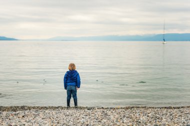 Bulutlu bir günde göl kenarında oynarken küçük çocuk