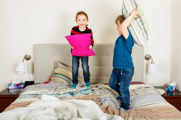 Dos niños adorables teniendo pelea de almohadas en la cama —  Fotos de Stock