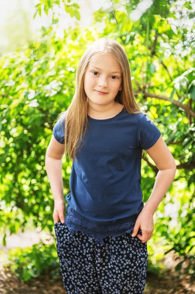 Retrato de uma linda menina de 7 anos de idade no parque em um dia ensolarado, vestindo camisa azul — Fotografia de Stock
