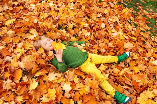 Ritratto autunnale di un simpatico bambino di 4 anni che gioca con foglie gialle nel parco, indossa pantaloni gialli, pullover verde e scarpe — Foto Stock