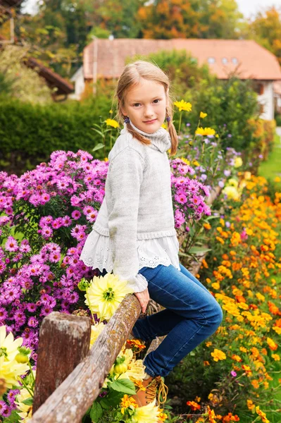 Outdoor portrait of a cute little girl of 8 years old, sitting on a fence, wearing warm grey pullover — Stock Photo, Image