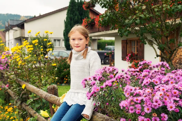 Outdoor portrait of a cute little girl of 8 years old, sitting on a fence, wearing warm grey pullover — Stock Photo, Image