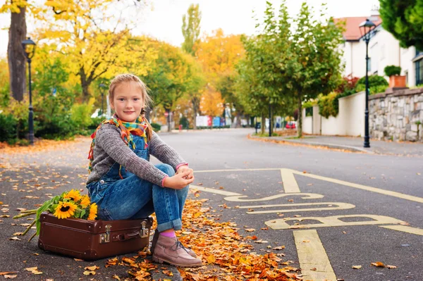 Jesień portret ładny blond dziewczynka 8 lat, na sobie ciepły sweter, denim kombinezon i beżowe buty, siedząc na starego rocznika walizki — Zdjęcie stockowe