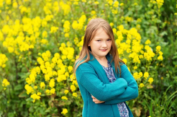 Außenporträt eines niedlichen kleinen Mädchens, das in einer Landschaft mit Blumen spielt und eine warme smaragdgrüne Strickjacke trägt — Stockfoto