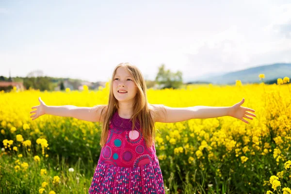 Outdoor portrait of a cute little girl playing with flowers in a countryside, arms wide open — Stock Photo, Image