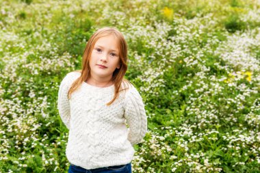 Beyaz sıcak örme kazak giyen bir alanda oynayan sevimli küçük Kızıl saçlı kız
