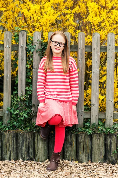 Outdoor portrait of a cute little girl in glasses, leaning on a fence — Stock Photo, Image