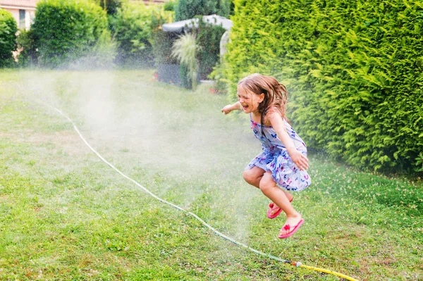 Criança brincando com aspersor de jardim, pulando — Fotografia de Stock