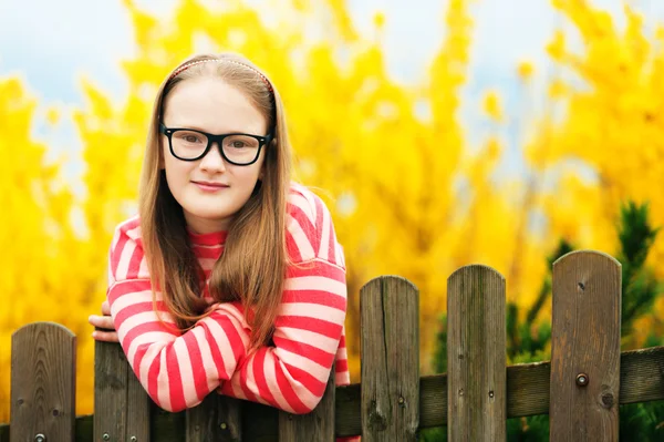 Portrait extérieur d'une jolie petite fille en lunettes, appuyée sur une clôture — Photo