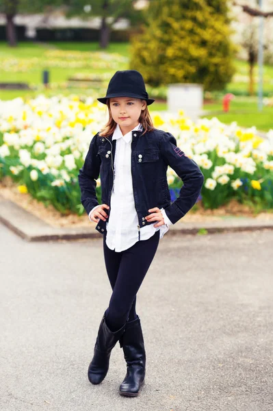 Petite fille mignonne de 7-8 ans jouant dans le parc de printemps, portant un ensemble élégant noir de veste noire, leggings, chapeau, bottes et chemisier blanc — Photo