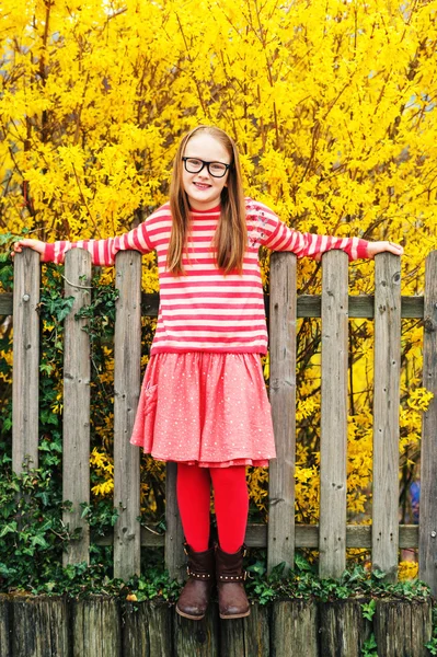 Outdoor portrait of a cute little girl in glasses, leaning on a fence — Stock Photo, Image