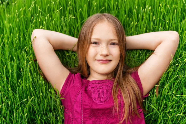 Young little girl resting outdoors. Close up outdoor portrait of adorable little girl of 8-9 years old laying on fresh lavender grass — Stock Photo, Image