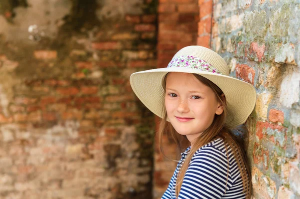 Ritratto da vicino all'aperto di una graziosa bambina di 8-9 anni, con cappello, in piedi contro un vecchio muro di mattoni — Foto Stock