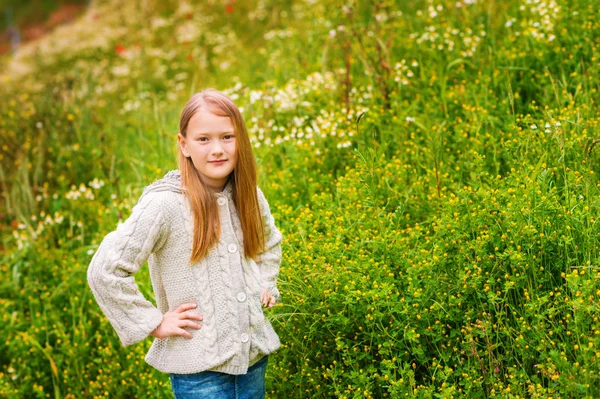 Retrato ao ar livre de adorável menina de 8-9 anos de idade, vestindo jaqueta de malha bege, posando em campo verde — Fotografia de Stock