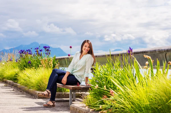 Porträt einer jungen brünetten Frau, die sich im Freien ausruht und auf der Bank am See sitzt — Stockfoto
