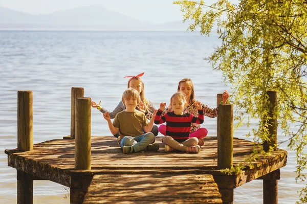 4 kinderen spelen door het meer, vier kinderen mediteren op de pier, getinte afbeelding — Stockfoto