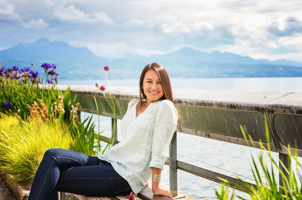 Portret van jonge brunette vrouw buitenshuis rusten, zittend op het bankje aan het meer — Stockfoto