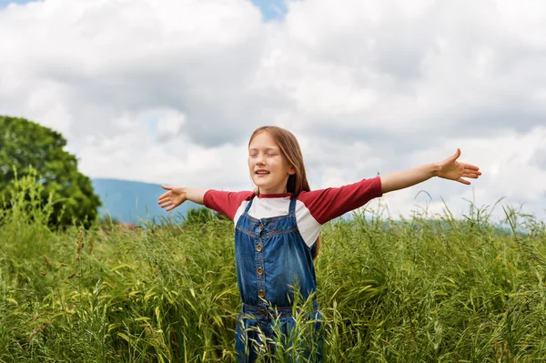 Bambina che gioca nel campo di grano verde in estate, indossa t-shirt e tuta rossa e bianca, braccia spalancate — Foto Stock