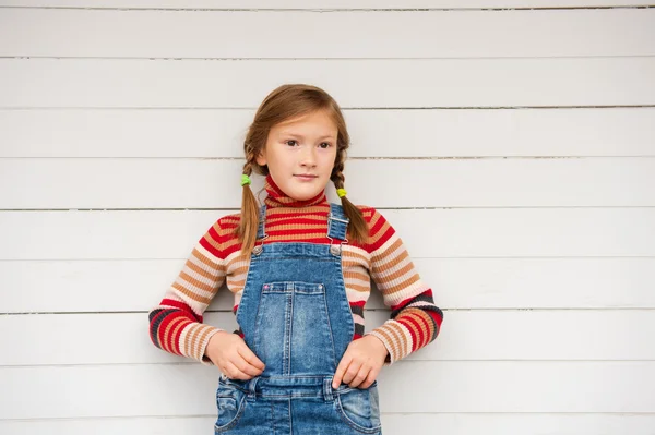 Ritratto di moda di una bambina carina sullo sfondo bianco, indossando pullover girocollo a righe e tuta in denim — Foto Stock