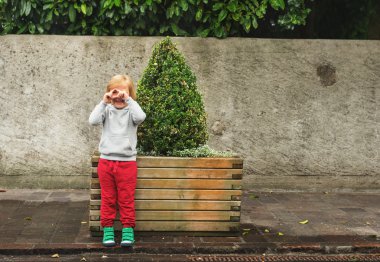 Fashion portrait of adorable toddler boy wearing grey sweatshirt, red trainings and green shoes. Kid pretending taking pictures with his hands clipart
