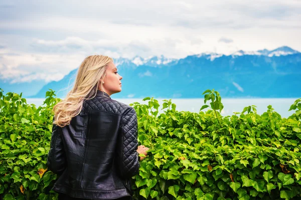 Portrait extérieur de belle femme blonde vêtue d'une veste en cuir noir, admirant le lac Léman dans la région de Lavaux, vue de dos — Photo