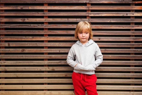 Fashion portrait of adorable toddler boy wearing grey sweatshirt, standing against wooden background — Stock Photo, Image