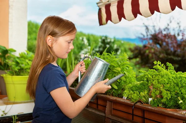 Entzückendes kleines Mädchen, das an einem schönen sonnigen Tag Pflanzen auf dem Balkon gießt — Stockfoto