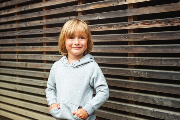 Portret mody uroczego chłopca ubranego w szarą bluzę, stojąc na drewnianym tle — Zdjęcie stockowe