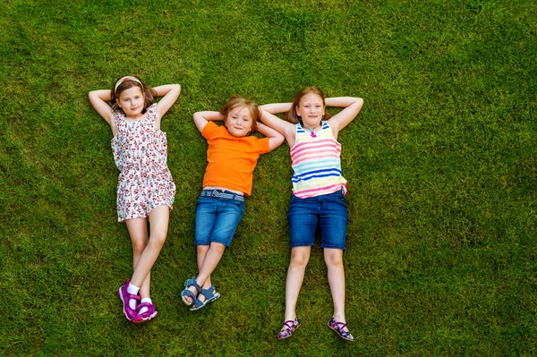 Crianças felizes se divertindo ao ar livre. Crianças brincando no parque de verão. Menino e duas meninas deitado na grama fresca verde — Fotografia de Stock