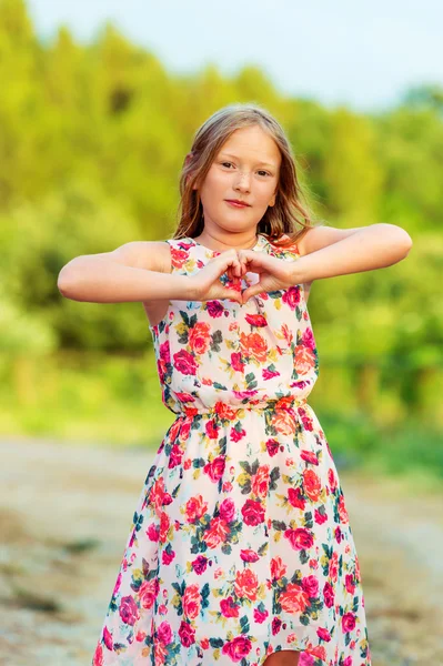 Retrato ao ar livre de uma menina bonito de 8 anos de idade fazendo forma de coração por suas mãos. Menina bonita brincando ao ar livre ao pôr do sol — Fotografia de Stock