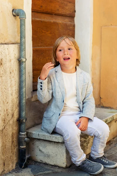 Retrato de moda ao ar livre de um menino bonito de 5 anos, vestindo jaqueta cinza e calças brancas — Fotografia de Stock