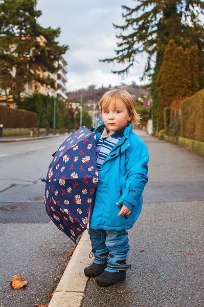 Cute toddler boy with umbrella playing outdoors on a rainy day, wearing blue jacket — Stock Photo, Image