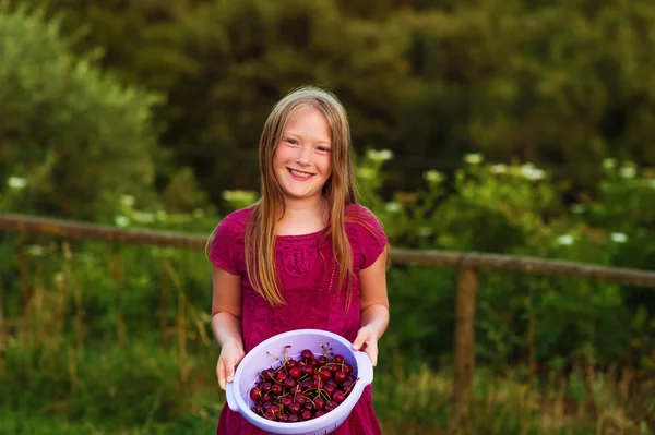 Portrait extérieur d'une joyeuse petite fille rieuse tenant un bol avec une cerise fraîche — Photo