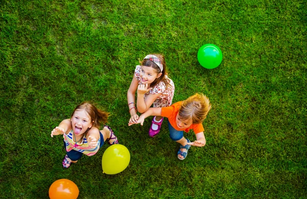 Três crianças pequenas felizes que jogam com balões coloridos ao ar livre, vista superior — Fotografia de Stock