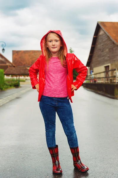 Retrato vertical ao ar livre de uma menina bonita de 8-9 anos de idade em um dia nublado, vestindo jaqueta de chuva vermelha brilhante — Fotografia de Stock